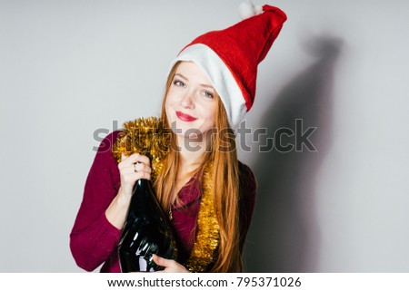 red-haired happy girl in a New Year's cap celebrates Christmas, keeps a bottle of champagne