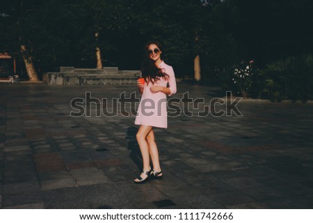 Red-haired hipster girl in pink dress and sunglasses with a glass of coffee in the city.