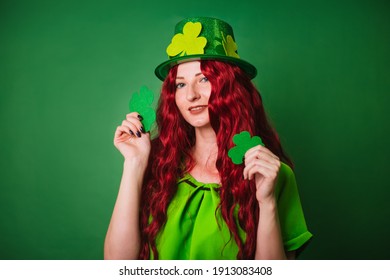 A red-haired long-haired girl on a green background holds a three-leaved tree in her hands. Celebrates st patrick's day. photo in studio