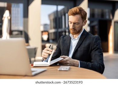 Red-haired man making notes in organizer while working outside