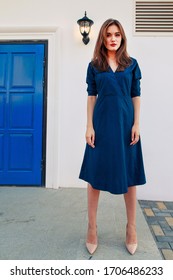 Red-haired model posing at the blue door in a dark blue dress