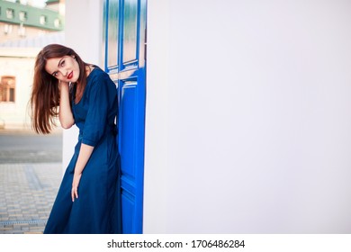 Red-haired model posing at the blue door in a dark blue dress