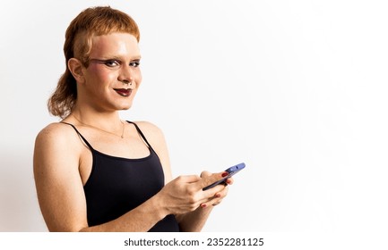 A red-haired non-binary person is posing on a white background with a mobile phone while looking at the camera happily. Concept of online dating, meeting people of the same sex. LGTBI advertising.