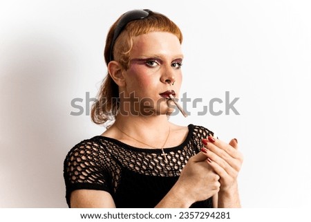 A red-haired non-binary person is posing on a white background. The man looks at the camera while lighting a cigarette. Concept of people is not identified with any gender.