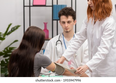 A Red-haired Nurse Puts A Blood Pressure Monitor On A Young Patient's Arm. Primary Care Physician. Doctor's Office