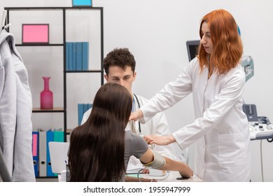 A Red-haired Nurse Puts A Blood Pressure Monitor On A Young Patient's Arm. Primary Care Physician. Doctor's Office