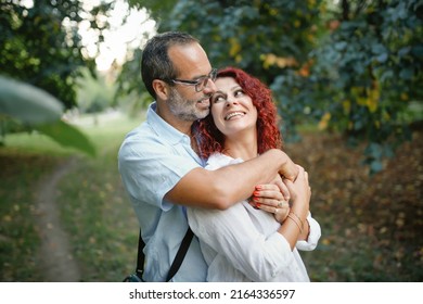 red-haired pretty woman hugs slender man with glasses. Cute middle aged european couple hugging in the park