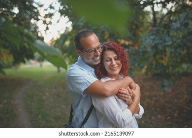 red-haired pretty woman hugs slender man with glasses. Cute middle aged european couple hugging in the park