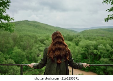 a red-haired woman with beautiful, well-groomed, long hair stands with her back to the camera and enjoys the view of the forest. High quality photo - Shutterstock ID 2165255891