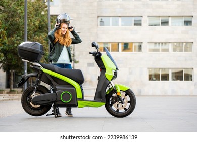 red-haired woman puts on her helmet next to her motorbike parked on the street