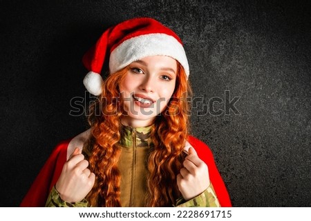 A red-haired woman in a Santa Claus costume and a red hat. Portrait happy girl in a military army uniform on a black dark background. Concept of Christmas or New Year. Stock photo © 
