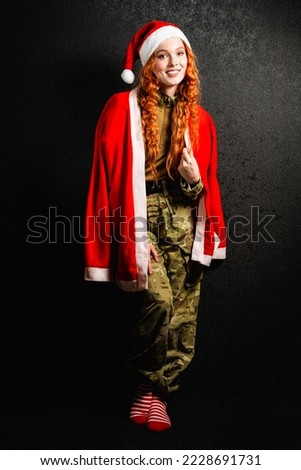 A red-haired woman in a Santa Claus costume and a red hat. Portrait of a happy girl in a military army uniform on a black dark background. Concept of Christmas or New Year. Stock photo © 