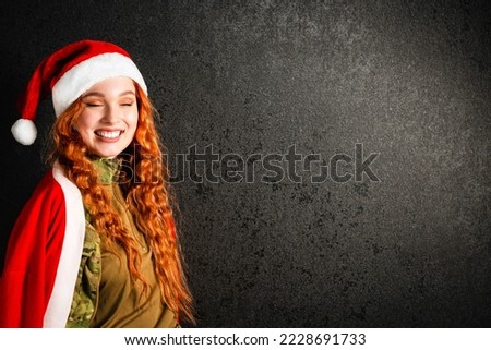 A red-haired woman in a Santa Claus costume and a red hat. Happy girl in a military army uniform on a black dark background. Concept of Christmas or New Year. Stock photo © 