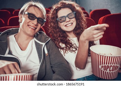 Red-haired woman smiles and shows something to the guy in the cinema. A man and a woman came to the cinema together. 