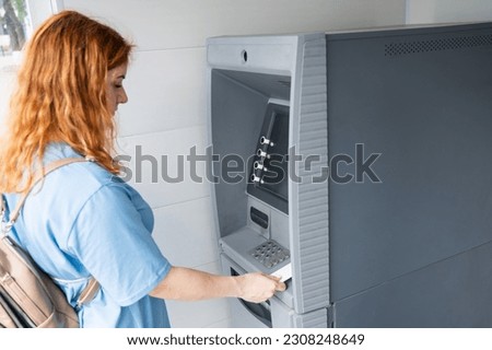 Red-haired woman using an ATM with contactless nfs access. 