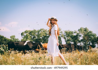 Red-haired woman walking on a field with cows,red-haired girl in a field of wheat in a white dress smiles a lovely smile , a perfect picture for advertising in the style lifestyle - Shutterstock ID 497949295