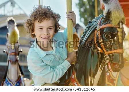 Redhead boy in the foreground of the camera rides a black horse at the special carousel. Healthy and cheerful smile of the child.