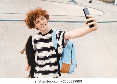 Redhead curly positive high school pupil student teen boy guy teenager skater in casual with backpack holds skateboard smart phone taking selfie shot against in city skate park riding on ramp - Powered by Shutterstock