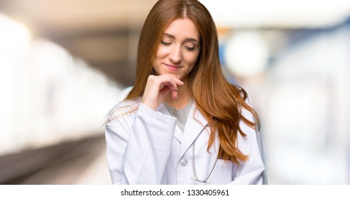 Redhead Doctor Woman Looking Down With The Hand On The Chin In The Hospital