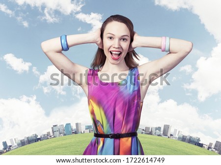 Redhead european girl closing her ears with hands. Charming lady in bright colorful dress and bracelets on background cityscape panorama. Portrait of happy young woman singing and smiling broadly