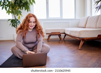 Redhead Fat Woman Waiting The Lesson By Online Personal Trainer, Using Laptop. Home Training, Technology And Diet. Overweight Female Having Rest, Going To Do Yoga Exercises Sitting On Fitness Mat