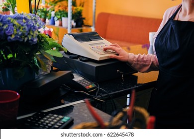 Redhead Female Flower Seller Using Cash Register In A Market Shop.