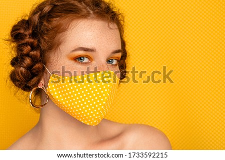 Redhead freckled woman wearing stylish handmade protective yellow polka dot cloth mask. Fashion during quarantine of coronavirus outbreak. Copy, empty space for text
