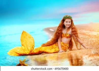 Redhead girl beautiful Siren Mermaid . Mermaid girl with gold tail put feet in water.