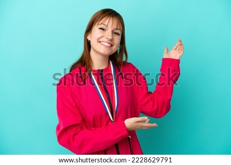 Redhead girl with medals isolated o blue background extending hands to the side for inviting to come Foto stock © 