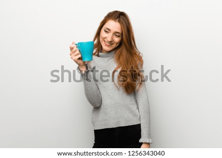 Redhead girl over white wall holding a hot cup of coffee
