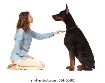 Redhead Girl Sitting On Her Knees In Front Of A Large Black Doberman  Dog, Isolated On White