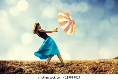Redhead girl with umbrella at windy field.