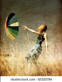 Redhead girl with umbrella at windy grass meadow. Photo in old color image style.