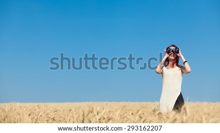 Redhead girl in white dress with binocular at wheat field.