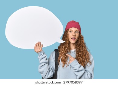 Redhead holding a comic speech bubble smiling and pointing aside, showing something at blank space.