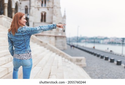 Redhead hungarian urban woman pointing into distance at Parliament building, Budapest, Hungary, widescreen