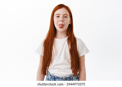 Redhead Little Girl With Long Natural Red Hair And Freckles, Shows Tongue Silly And Childish, Having Fun. Happy Kid With Ginger Hairdo Feeling Positive, White Background