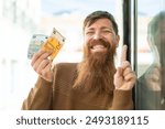 Redhead man with beard taking a lot of money at outdoors pointing up a great idea