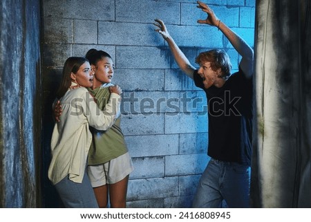 redhead man gesturing and scaring terrified multicultural female friends in escape room, quest