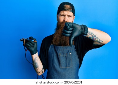 Redhead Man With Long Beard Tattoo Artist Wearing Professional Uniform And Gloves Looking Unhappy And Angry Showing Rejection And Negative With Thumbs Down Gesture. Bad Expression. 