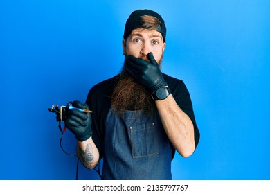 Redhead Man With Long Beard Tattoo Artist Wearing Professional Uniform And Gloves Shocked Covering Mouth With Hands For Mistake. Secret Concept. 