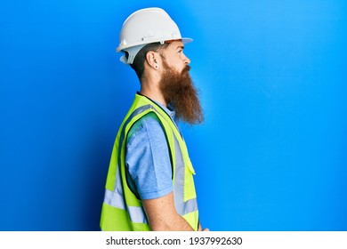 Redhead Man With Long Beard Wearing Safety Helmet And Reflective Jacket Looking To Side, Relax Profile Pose With Natural Face With Confident Smile. 