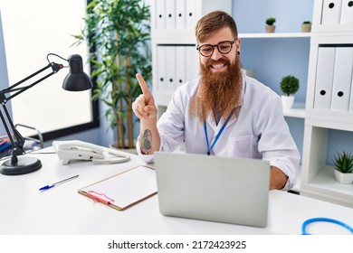 Redhead Man With Long Beard Wearing Doctor Uniform Working Using Computer Laptop Smiling Happy Pointing With Hand And Finger To The Side 