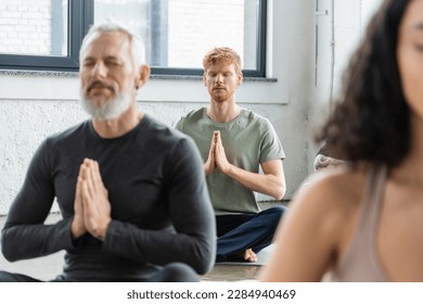 Redhead man meditating with anjali mudra near blurred people in yoga class - Powered by Shutterstock