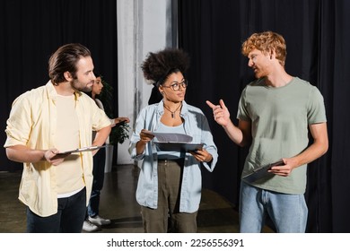 redhead man pointing with finger while talking to interracial students with screenplays in theater - Powered by Shutterstock