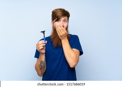 Redhead Man Shaving His Beard Over Isolated Blue Background With Surprise Facial Expression