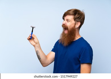 Redhead Man Shaving His Beard Over Isolated Blue Background