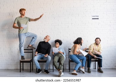 redhead man standing on chair and rehearsing near multiethnic actors sitting and waiting for casting - Powered by Shutterstock