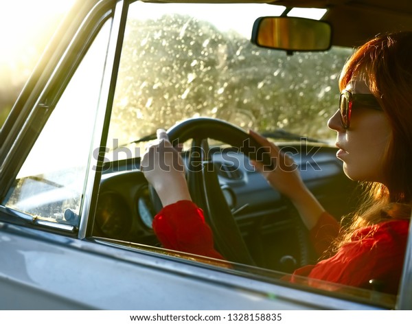 redhead middle age stylish woman driving the\
white retro aged car . sunny spring day.\
