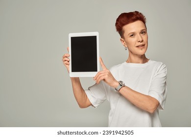 redhead non-binary person in white t-shirt showing digital tablet with blank screen on grey backdrop - Powered by Shutterstock